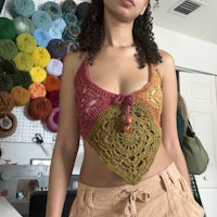 a woman wearing a crocheted top standing in a room full of yarn