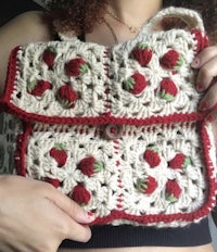 a woman is holding a crocheted bag with strawberries on it